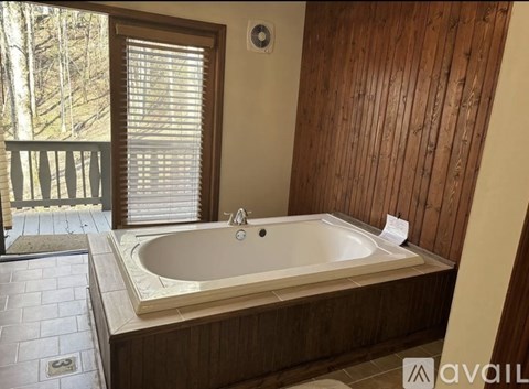 A bathroom with a large tub and a view of trees outside the window.