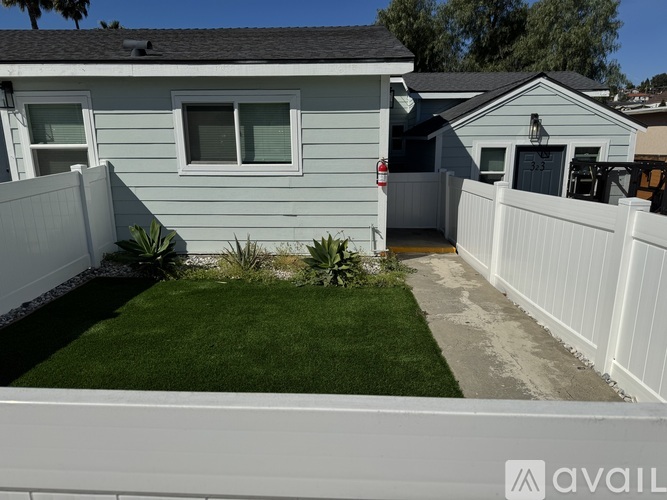 A house with a white fence and green plants in the front yard.