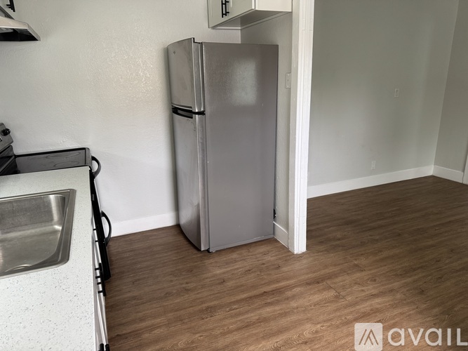 A small kitchen with a silver fridge and wooden flooring.