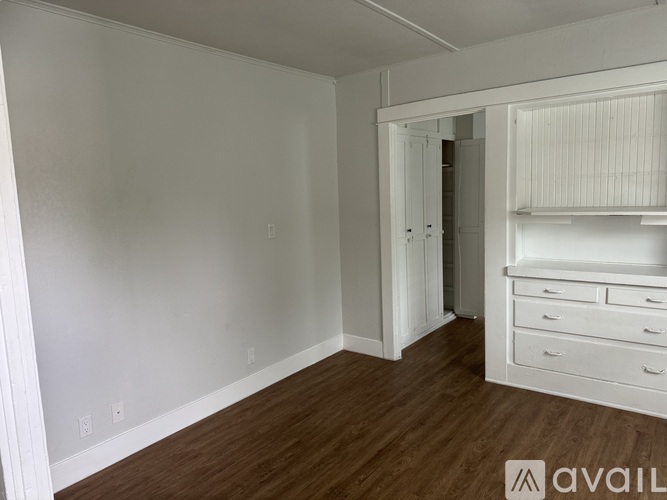 A room with white walls and wooden flooring, with a white wardrobe and a small white dresser.