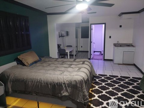 A bedroom with a bed, a ceiling fan, and a small kitchenette.