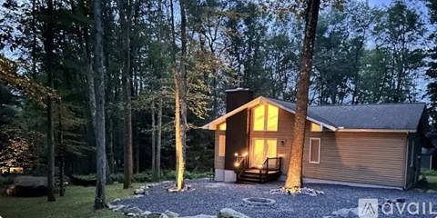 A house with a brown roof and a porch is surrounded by trees.