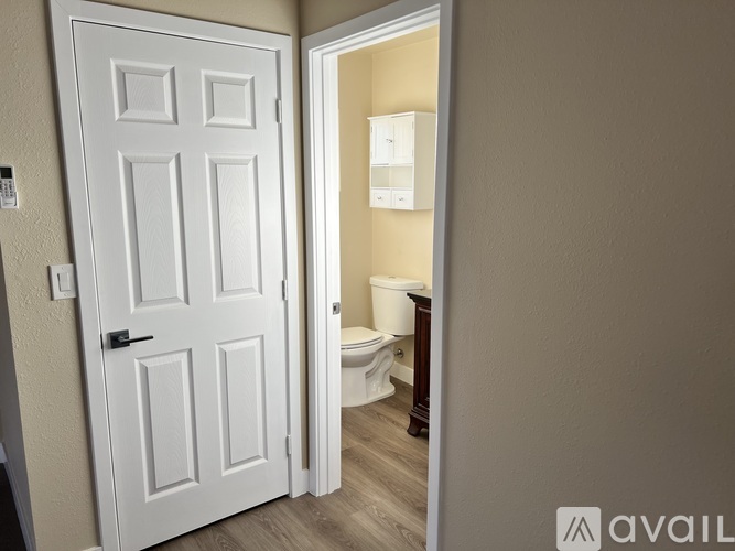 A white door is open to a bathroom with a toilet and a cabinet.
