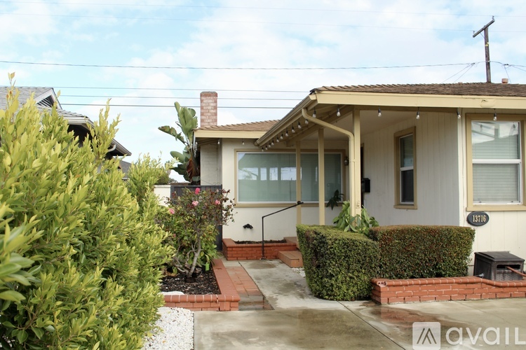 A house with a white exterior and a brown roof is surrounded by green bushes.