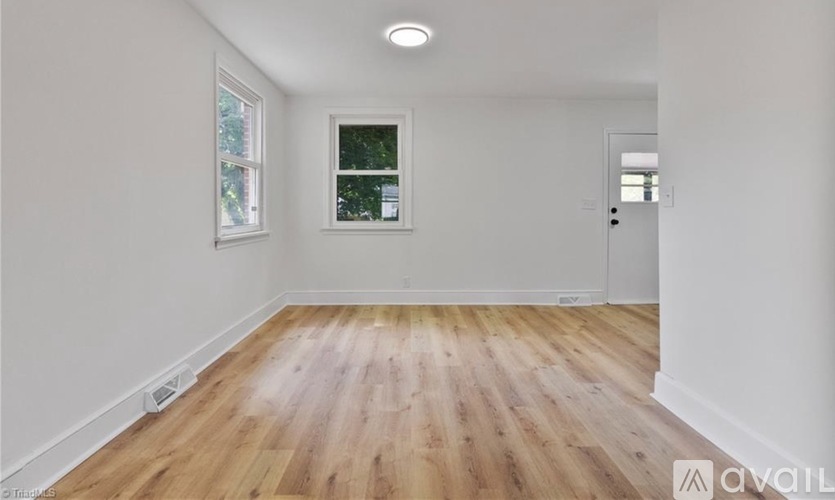 A room with wooden flooring and white walls, with a window and a door visible.