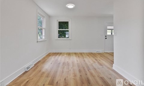 A room with wooden flooring and white walls, with a window and a door visible.