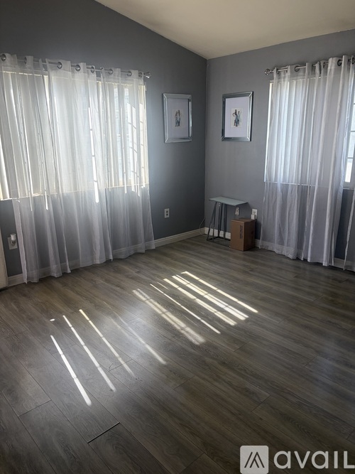 A room with wooden flooring and white curtains.