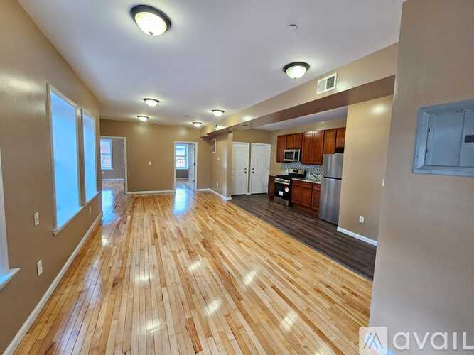 A spacious room with wooden flooring and a kitchen area in the background.