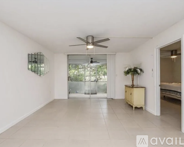 A spacious room with a ceiling fan and a sliding glass door leading to a balcony.