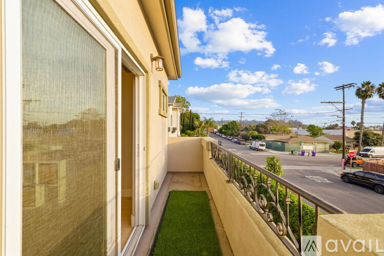 A balcony with a green lawn and a view of a street with cars and palm trees.