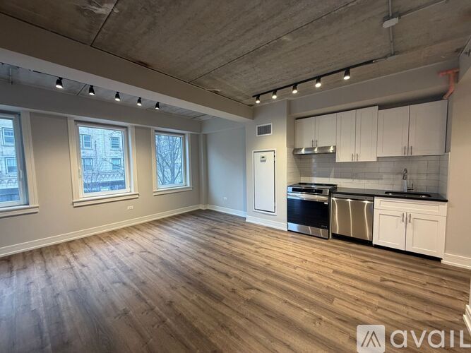 A spacious room with wooden flooring and a kitchen area with white cabinets.