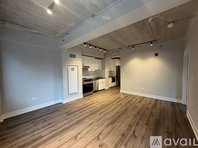 A spacious room with wooden flooring and a kitchen area in the background.