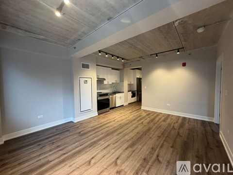 A spacious room with wooden flooring and a kitchen area in the background.