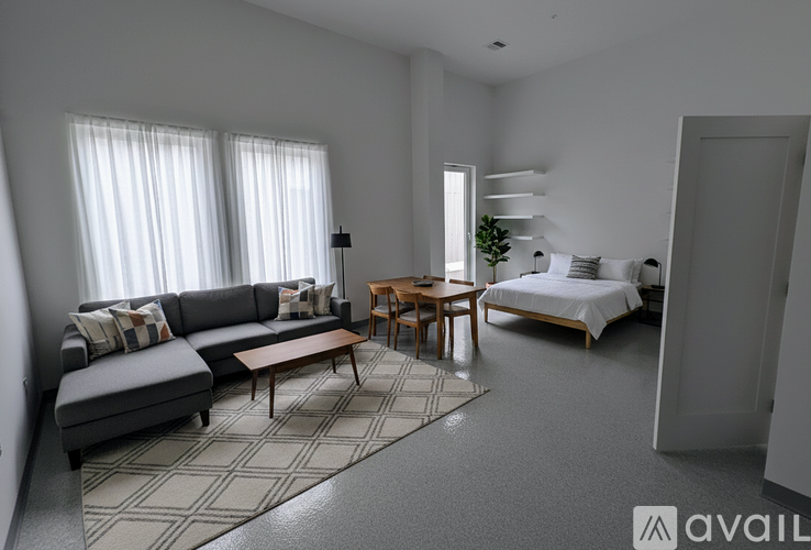 A modern living room with a grey sofa, a wooden coffee table, and a bed with white bedding.
