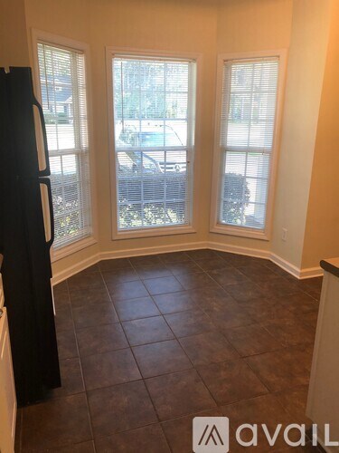 A kitchen with a black refrigerator and brown tiled flooring.