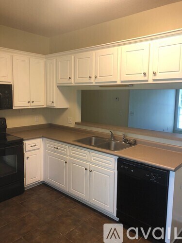 A kitchen with white cabinets and brown flooring.