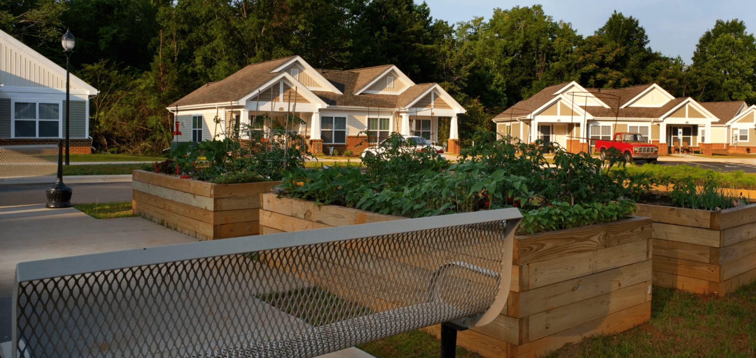 A park bench is in the foreground of a residential area with houses and trees in the background.