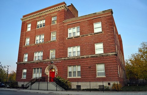 A red brick building with a red door and a black fence.