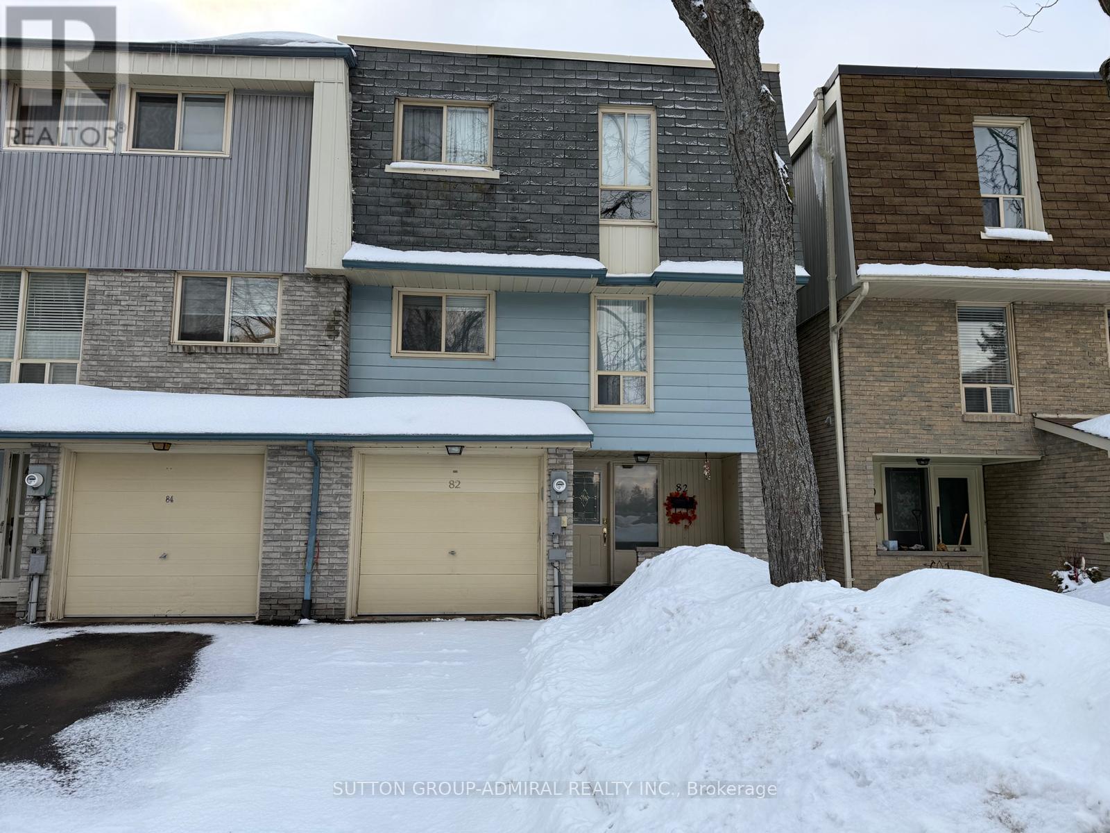 A snow-covered residential area with a house and a tree.