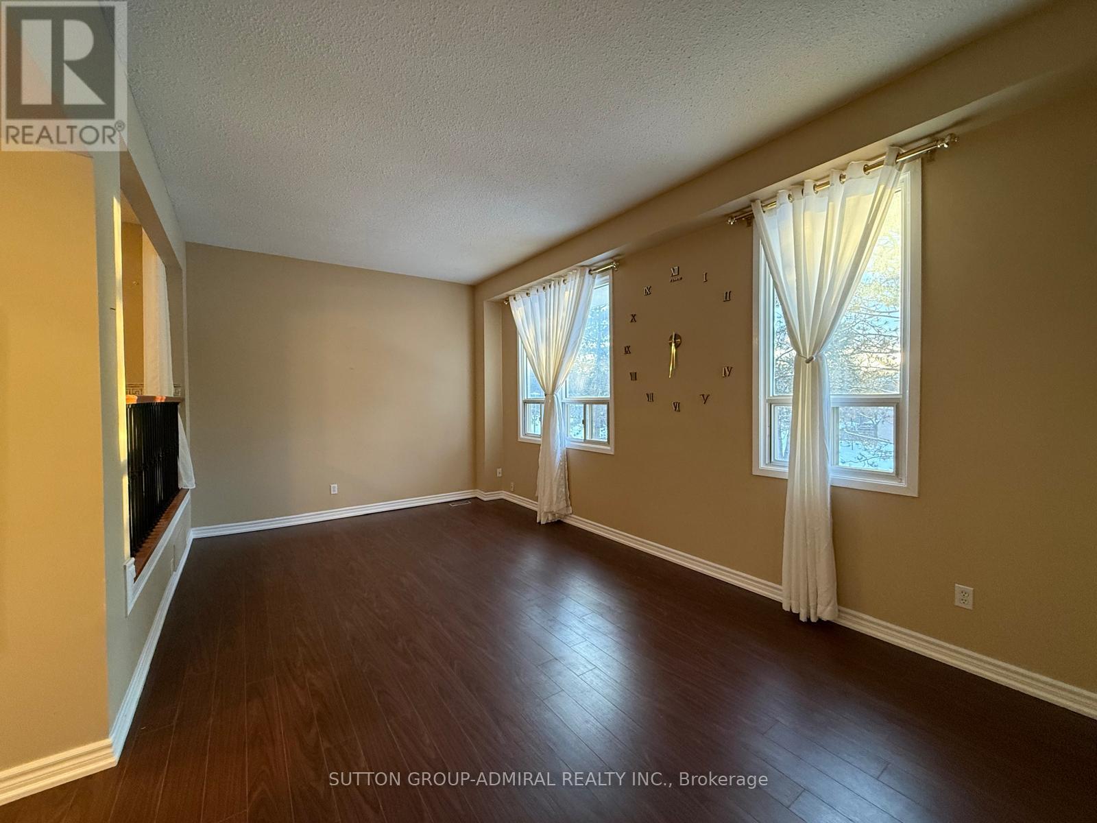 A spacious room with wooden floors and a large window with curtains.