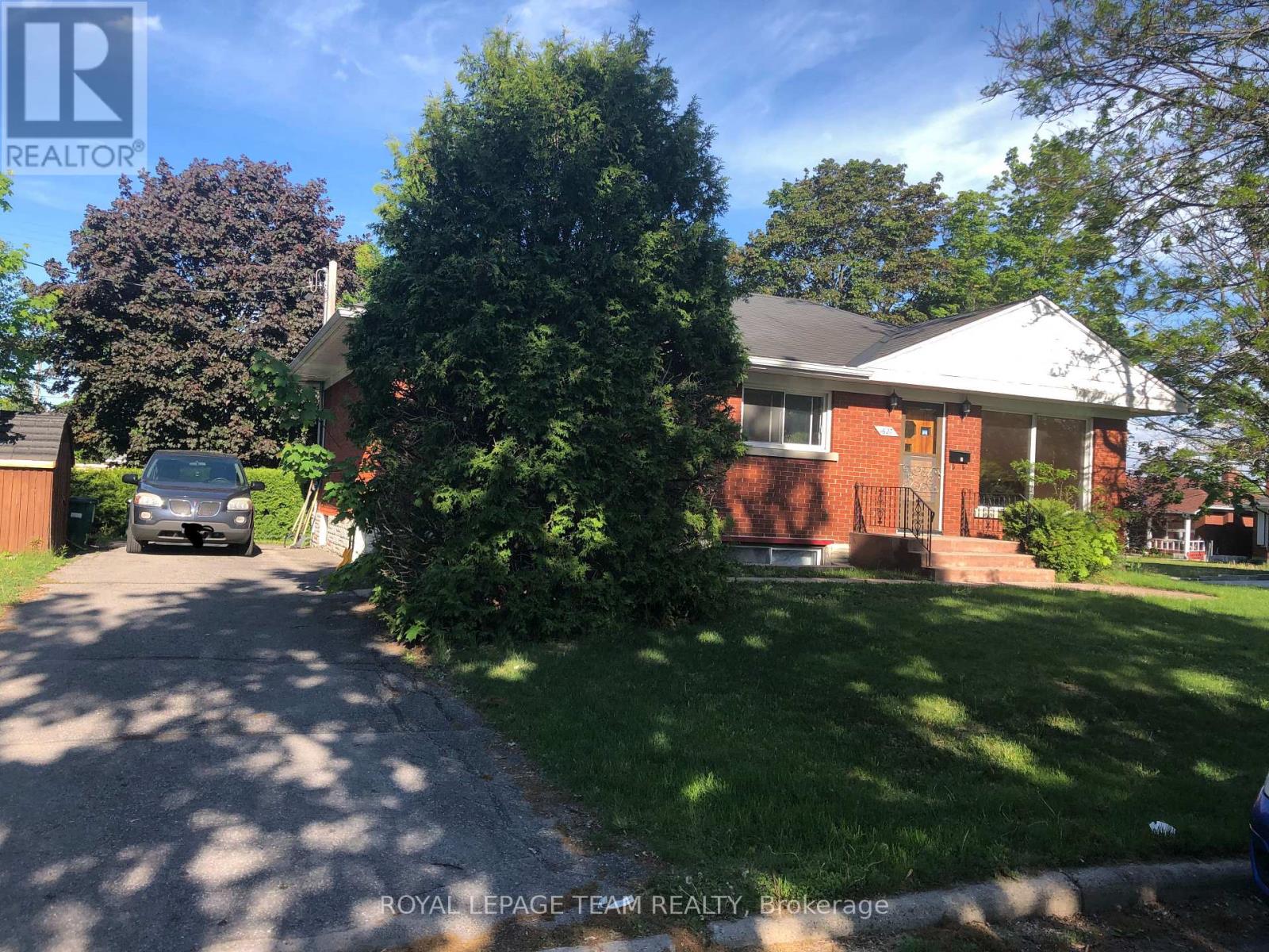 A house with a red door is surrounded by greenery and a car is parked in the driveway.