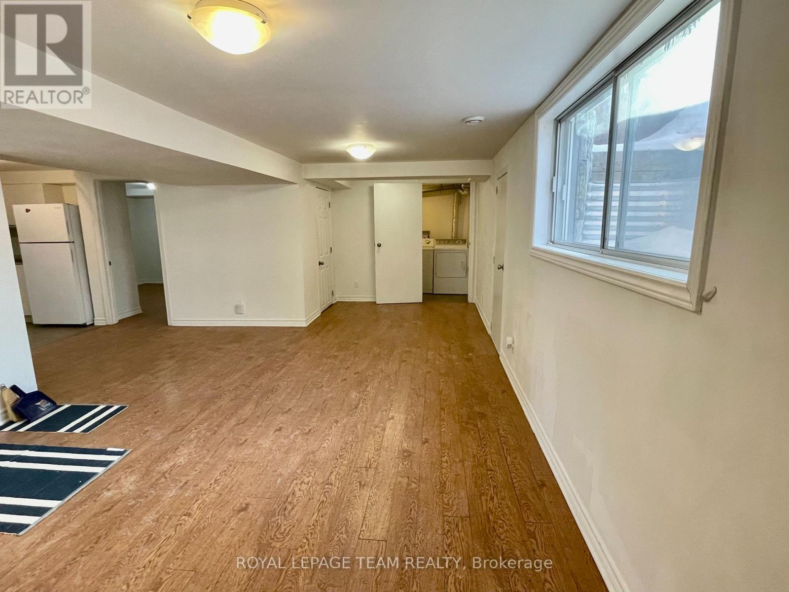 A room with wooden flooring and white walls, with a window on the right side.