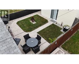 A patio with a table and chairs is surrounded by a grassy area and a house.