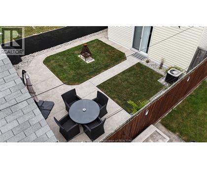A patio with a table and chairs is surrounded by a grassy area and a house.