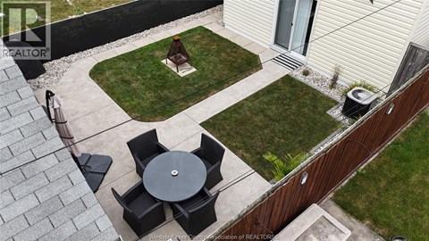 A patio with a table and chairs is surrounded by a grassy area and a house.
