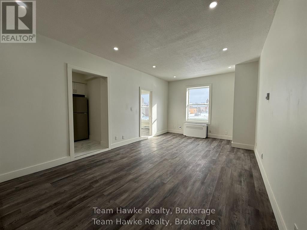 A spacious room with wooden flooring and white walls, with a window and a door visible.