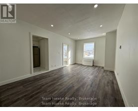 A spacious room with wooden flooring and white walls, with a window and a door visible.
