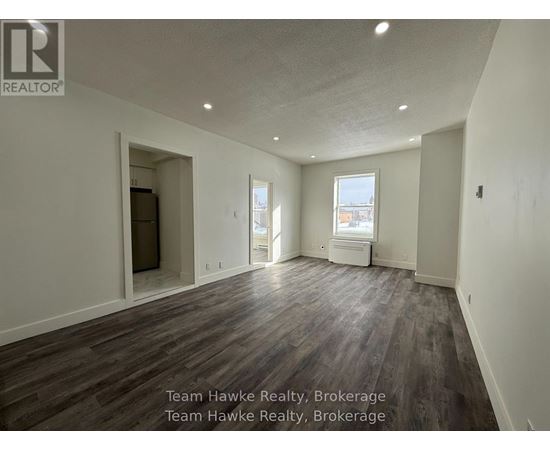 A spacious room with wooden flooring and white walls, with a window and a door visible.