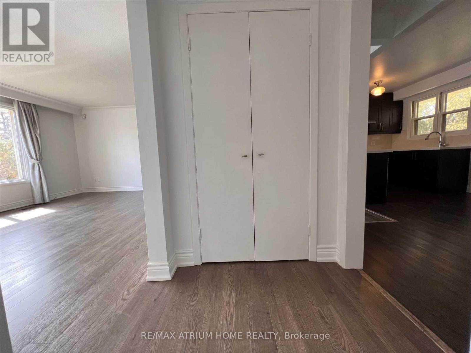 A white door in a room with wooden flooring and a window with curtains.