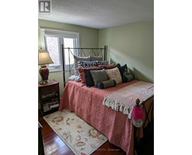 A bedroom with a bed covered in a pink comforter and a lamp on a nightstand.