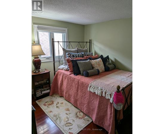 A bedroom with a bed covered in a pink comforter and a lamp on a nightstand.