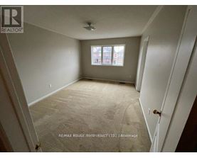 A room with a carpeted floor and a window with a view of a building outside.