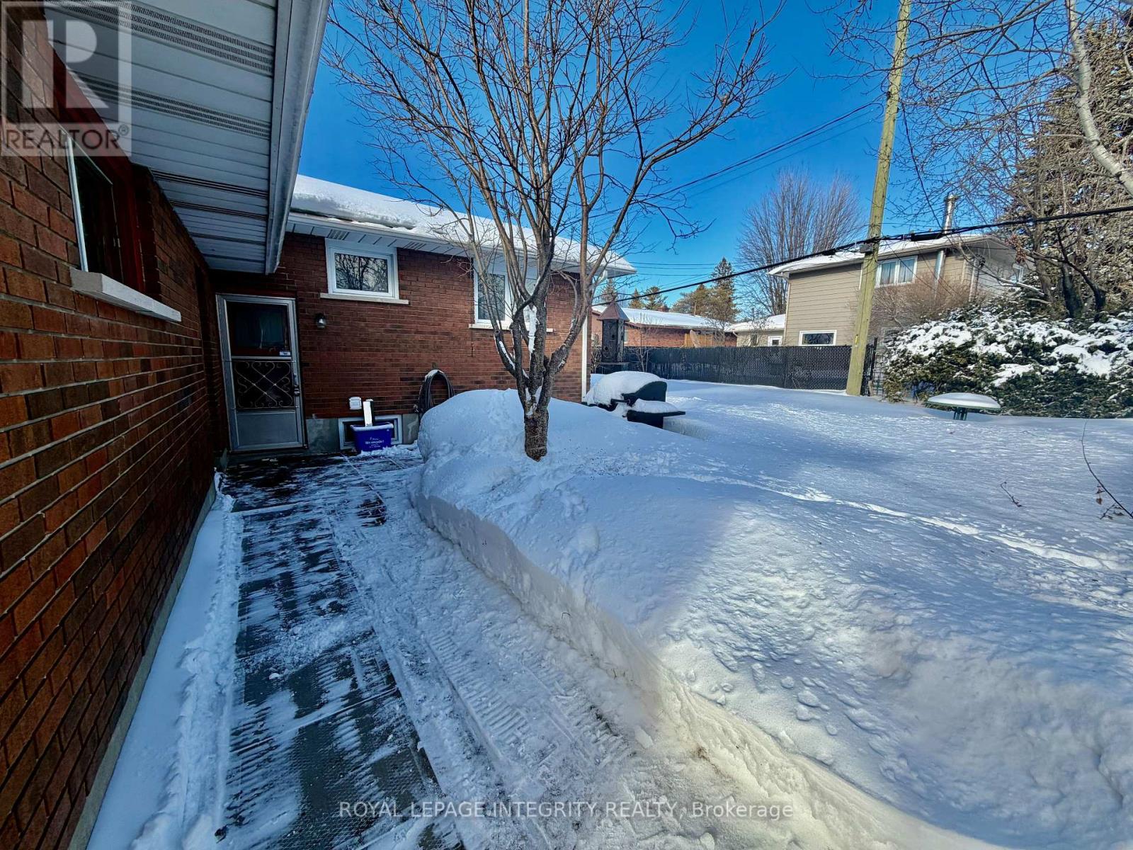 A snow-covered yard with a tree and a house in the background.