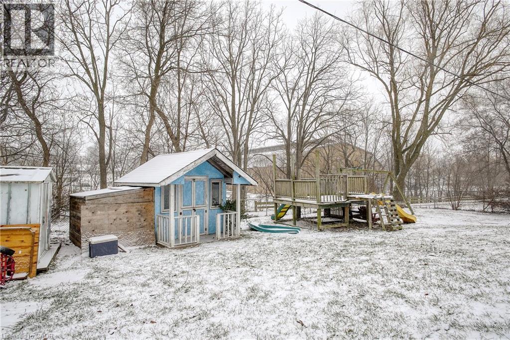 A blue shed sits in a snowy field with a deck and a hot tub nearby.