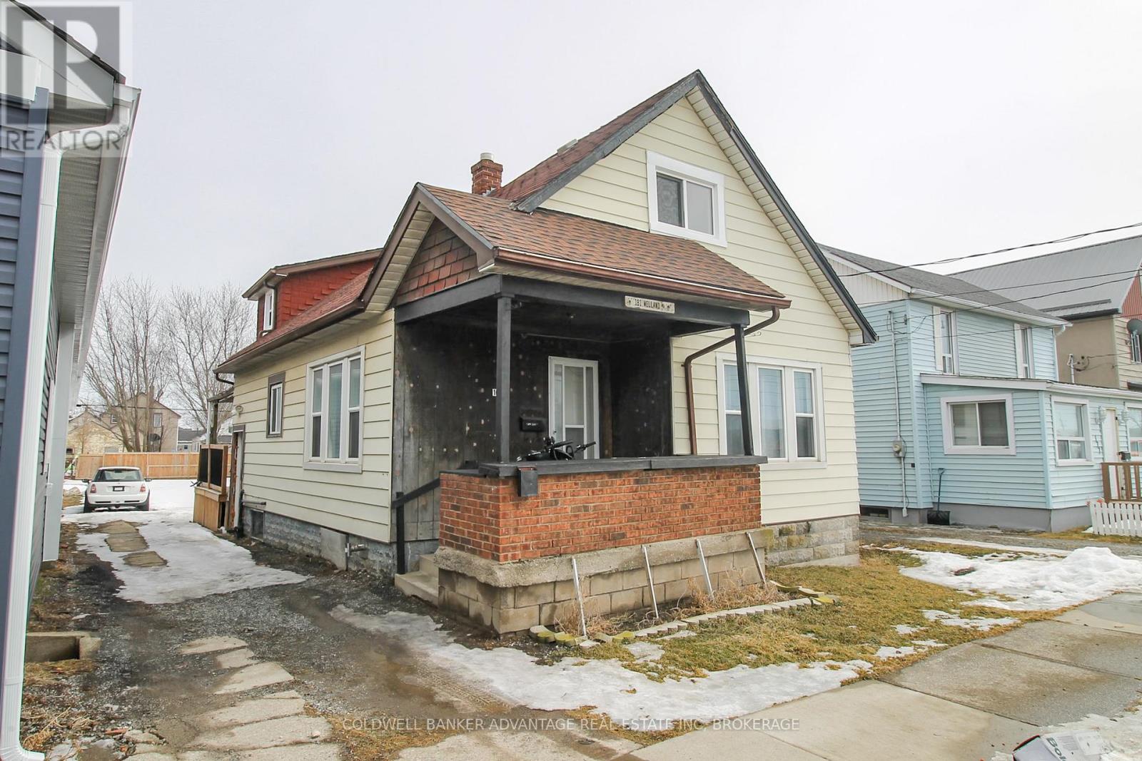A house with a porch and a brick chimney is surrounded by other houses.