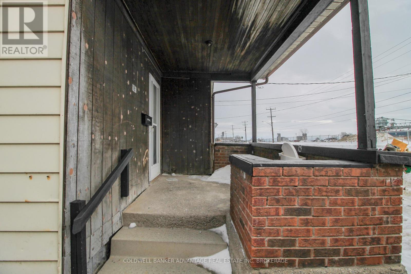A wooden porch with a brick pillar and a metal railing.