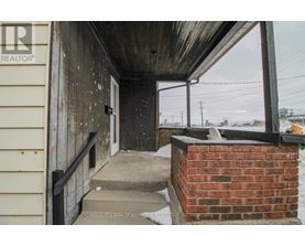 A wooden porch with a brick pillar and a metal railing.