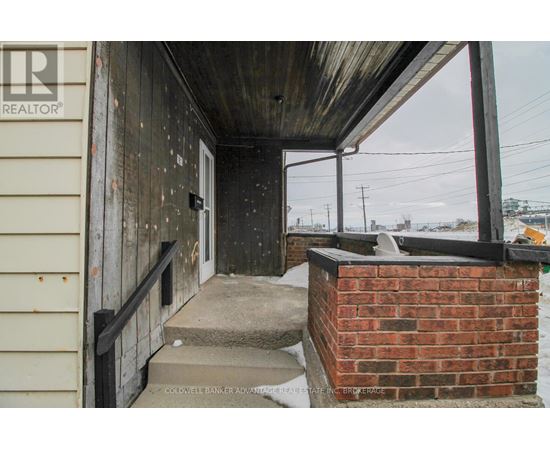 A wooden porch with a brick pillar and a metal railing.