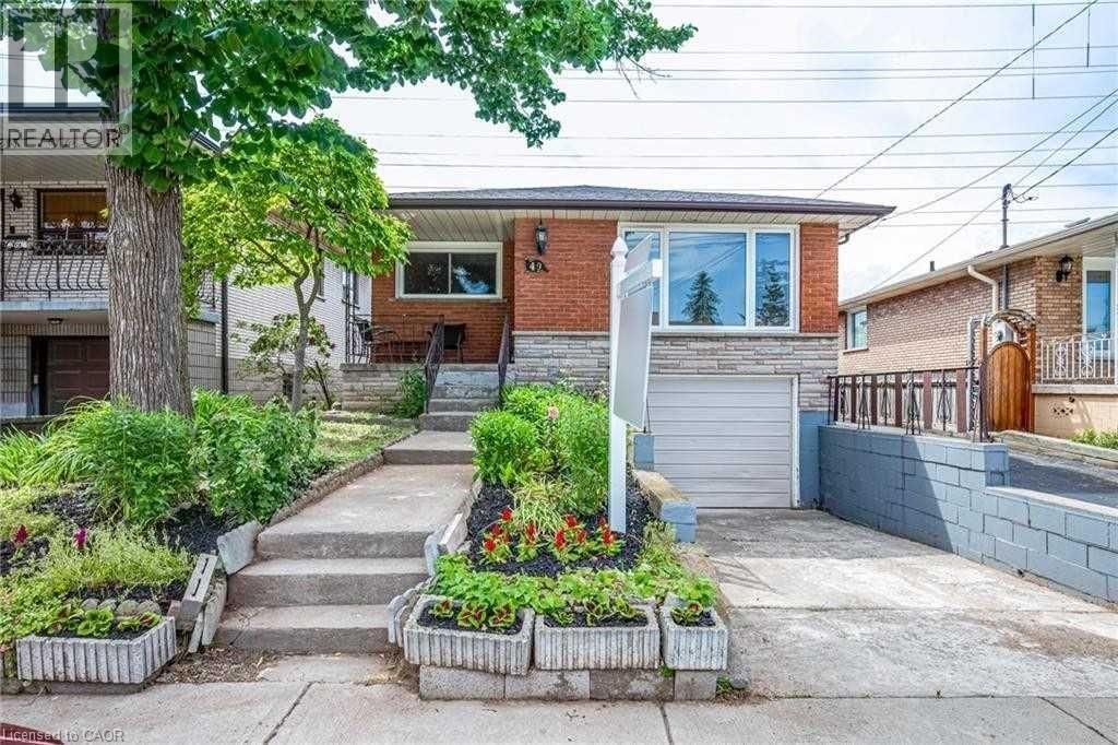 A house with a red brick exterior and a white garage door is surrounded by a garden with a variety of plants and flowers.