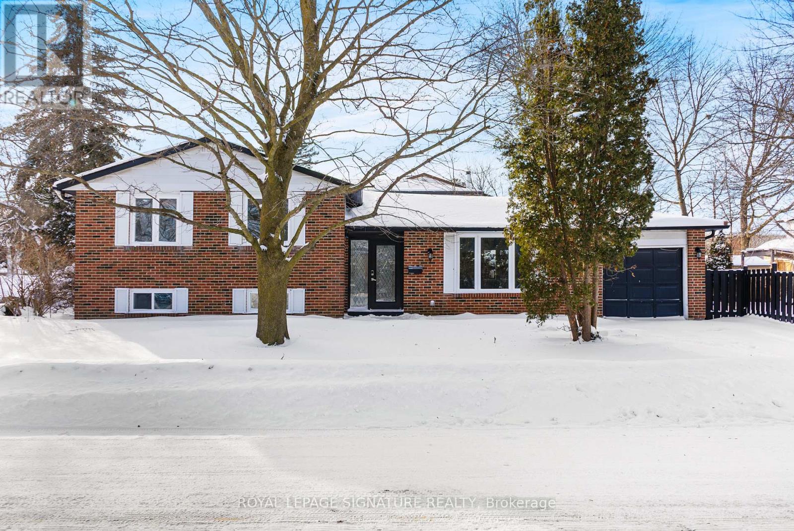 A house with a white garage door and a black door is surrounded by snow.