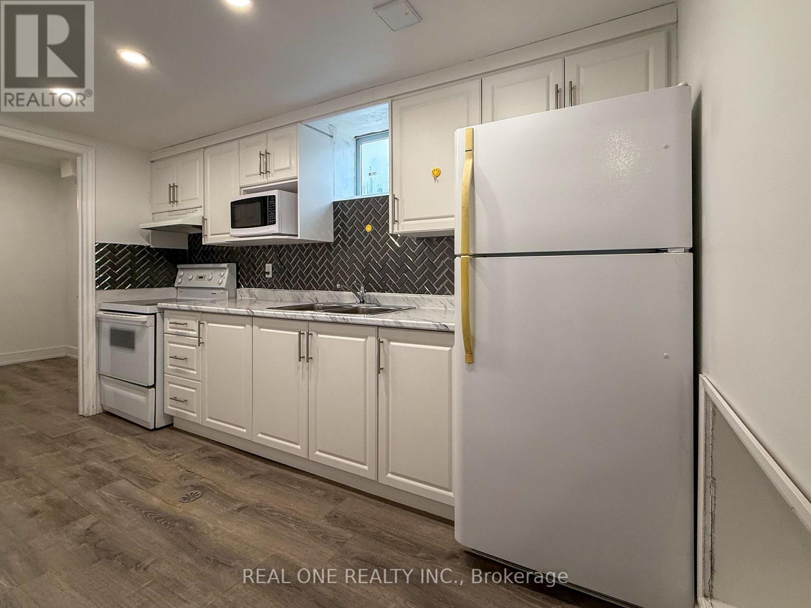 A white refrigerator stands in a kitchen with white cabinets and a black backsplash.