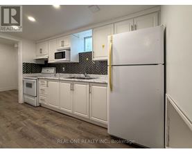 A white refrigerator stands in a kitchen with white cabinets and a black backsplash.