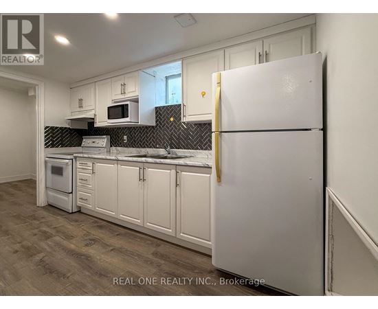 A white refrigerator stands in a kitchen with white cabinets and a black backsplash.