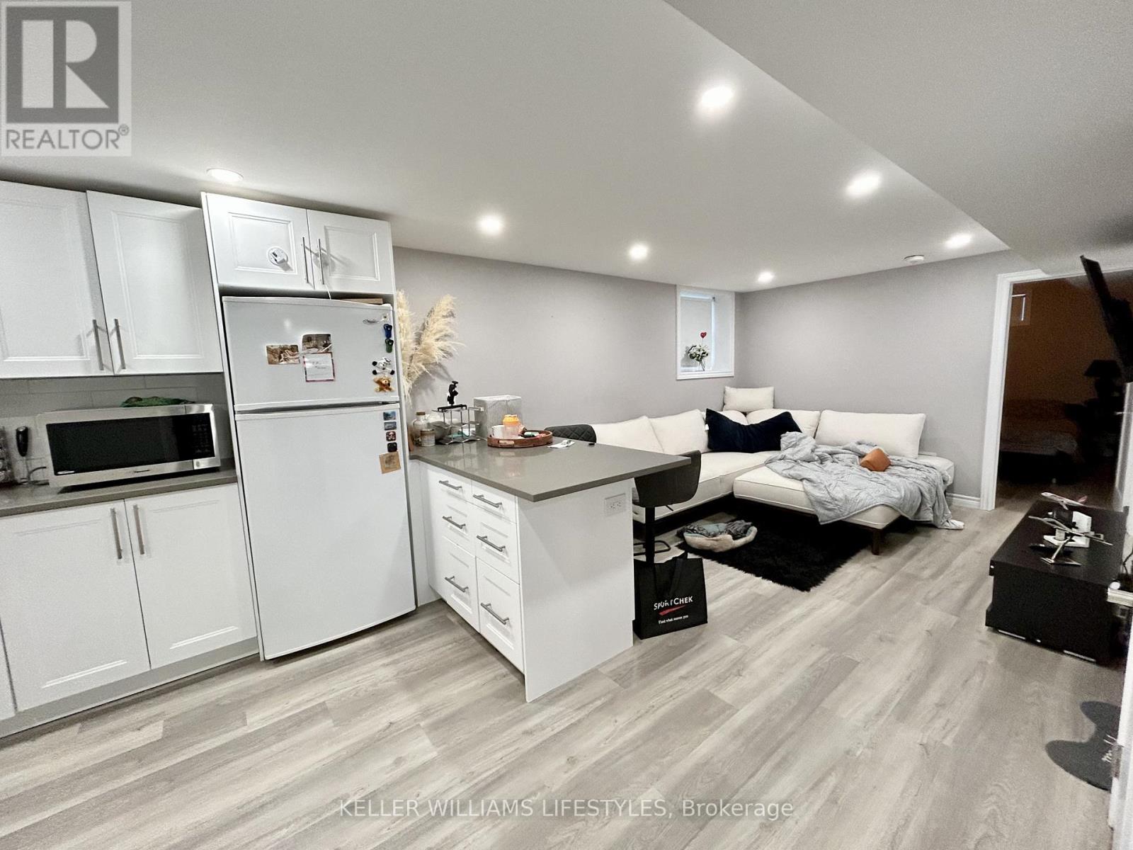 A well-lit kitchen with white cabinets and a refrigerator, a dining area with a table and chairs, and a living area with a couch and a coffee table.