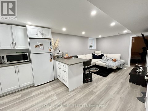 A well-lit kitchen with white cabinets and a refrigerator, a dining area with a table and chairs, and a living area with a couch and a coffee table.