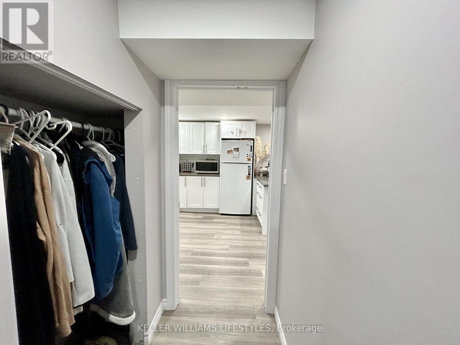 A hallway with clothes hanging on a rack and a kitchen in the background.